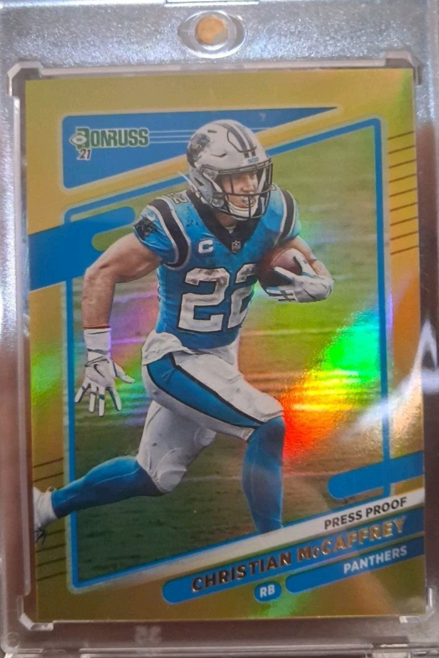 A collectible football trading card of Christian McCaffrey in a clear plastic protective sleeve, set against a neutral gray background.